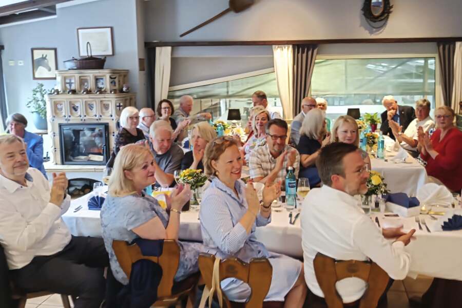 Personen sitzen an einer langen Tafel und schauen ins Bild