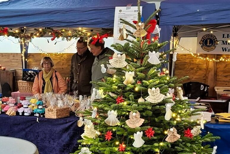 Tannenbaum geschmückt mit Notenengeln und Fröbelsternen im Hintergrund Lionsmitglieder am Stand